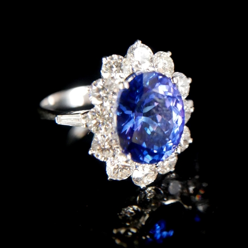 25 - AN 18CT WHITE GOLD, OVAL AAA TANZANITE AND ROUND BRILLIANT CUT DIAMOND CLUSTER RING.
(Size O).
