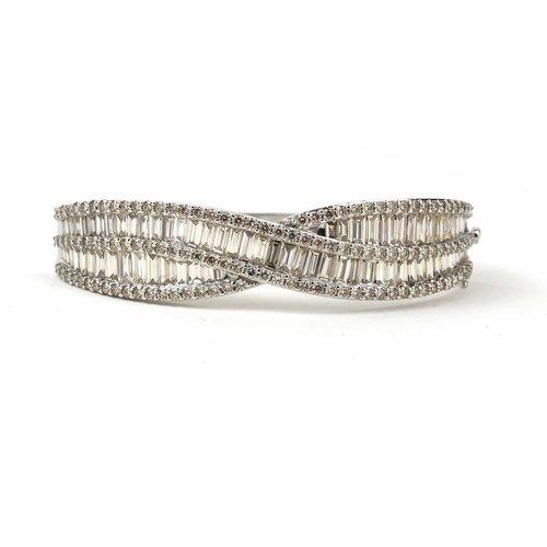 36 - AN IMPRESSIVE LARGE 9CT WHITE GOLD TWIST STYLE DIAMOND BANGLE, SET WITH BAGUETTE CUT AND ROUND BRILL... 