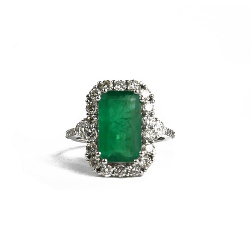 92A - AN 18CT WHITE GOLD EMERALD AND DIAMOND CLUSTER RING.  (Emerald 3.72ct, Diamonds 1.17ct)