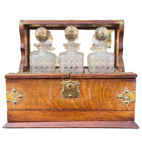 74 - A VICTORIAN WOODEN AND BRASS TANTALUS SET
Having three decanters and three port glasses. 
(h 31.5cm ... 