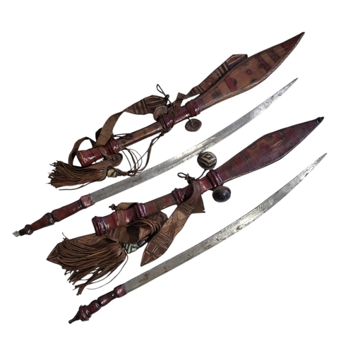 140A - TWO LATE 19TH/EARLY 20TH CENTURY WEST AFRICAN MANDINKA/MANDINGO LEATHER CLAD SWORDS.
(largest 71cm)