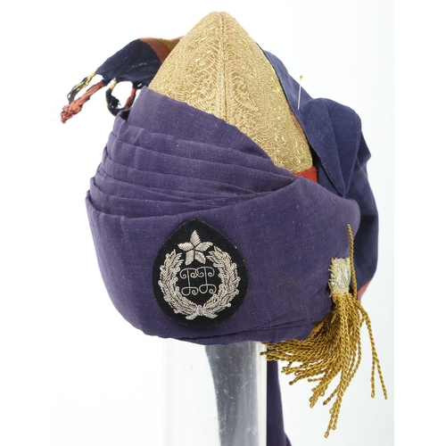 52 - Indian Turban, of recent manufacture, made from blue cloth with gilt embroidery and badge ( glued to... 
