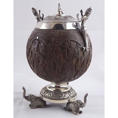 21 - A carved coconut covered pot having white metal handles, mounts and circular stand supported by thre... 