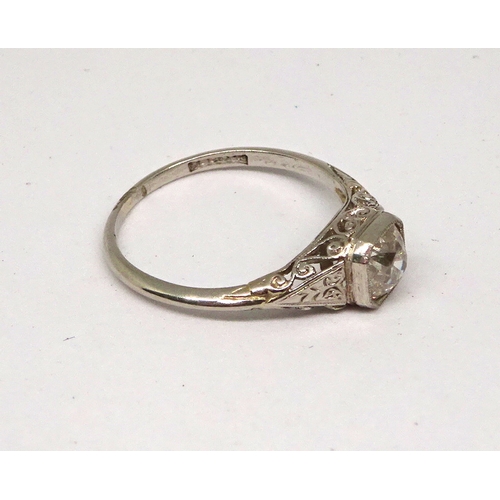 115 - A ring comprising an old mine cut white stone in a cushion shaped closed setting on openwork shoulde... 