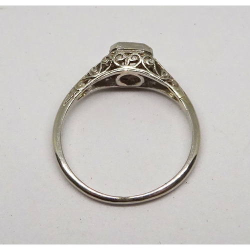 115 - A ring comprising an old mine cut white stone in a cushion shaped closed setting on openwork shoulde... 