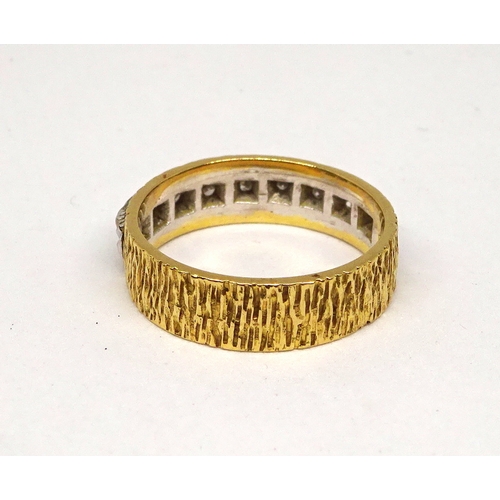 158 - A band ring comprising nine small brilliant cut white stones in a white metal setting on a bark text... 