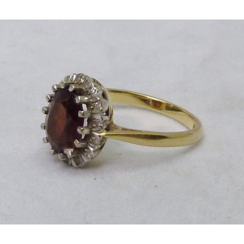 389 - A cluster ring comprising a central oval cut red stone surrounded by small white stones, yellow meta... 