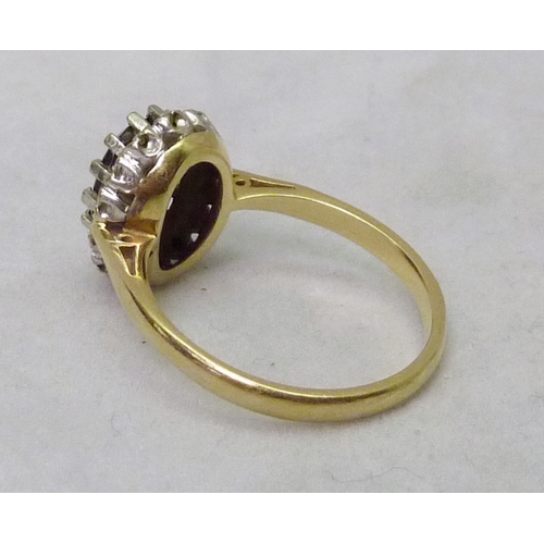 389 - A cluster ring comprising a central oval cut red stone surrounded by small white stones, yellow meta... 