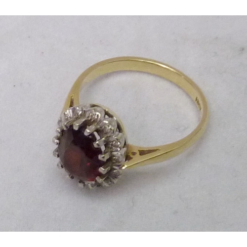 389 - A cluster ring comprising a central oval cut red stone surrounded by small white stones, yellow meta... 