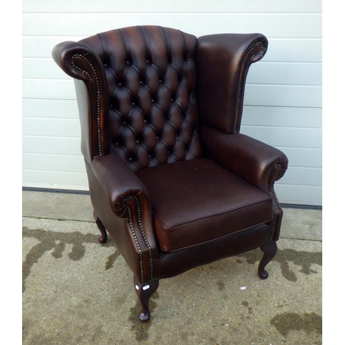 704 - A brown buttoned leather wingback armchair, plastic legs