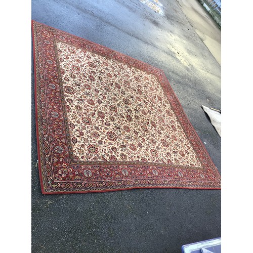 937 - A large machine made rug with beige centre and red border 275 x 272cm