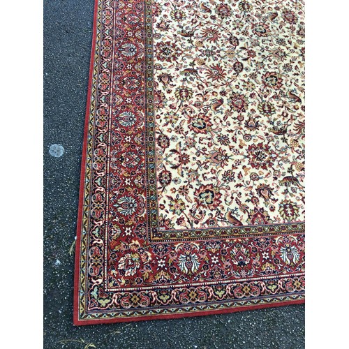 937 - A large machine made rug with beige centre and red border 275 x 272cm