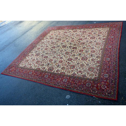 937 - A large machine made rug with beige centre and red border 275 x 272cm