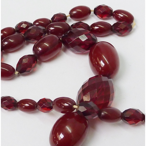 36 - A necklace comprising a string of alternating smooth and facet cut cherry coloured bakelite beads.  ... 