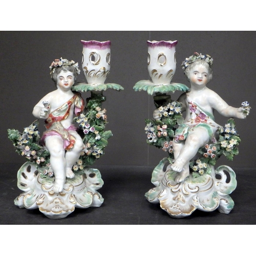 102 - A pair of floral encrusted cherub candlesticks; a taza stand having pierced basket and a lozenge sha... 