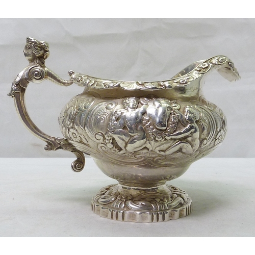 11 - A George III silver jug having repousse decoration incorporating scrolls, floral motifs and cherub a...
