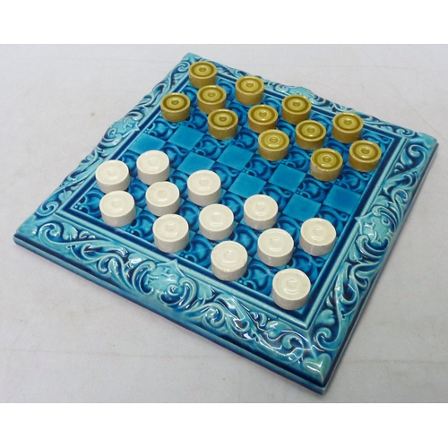 A Leeds Fireclay Co. Ltd draughts board and twenty-four matching draughts pieces, the board moulded with scrolling border and FLC motif, impressed THE LEEDS FIRECLAY Co. LTD WORTLEY LEEDS.  Board 209mm square.  A/F small chips to several counters.