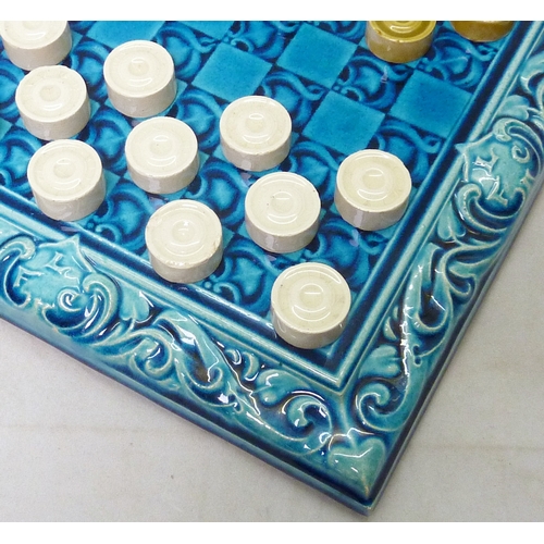 200 - A Leeds Fireclay Co. Ltd draughts board and twenty-four matching draughts pieces, the board moulded ... 