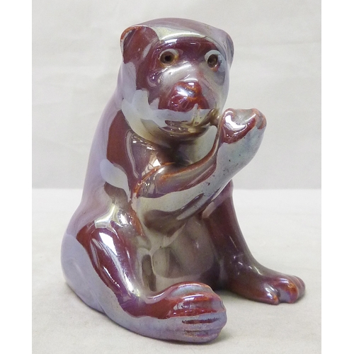 204 - A Burmantofts Faience robed monkey figure, lustre glaze in pink tones, glass bead eyes lacking, bear... 
