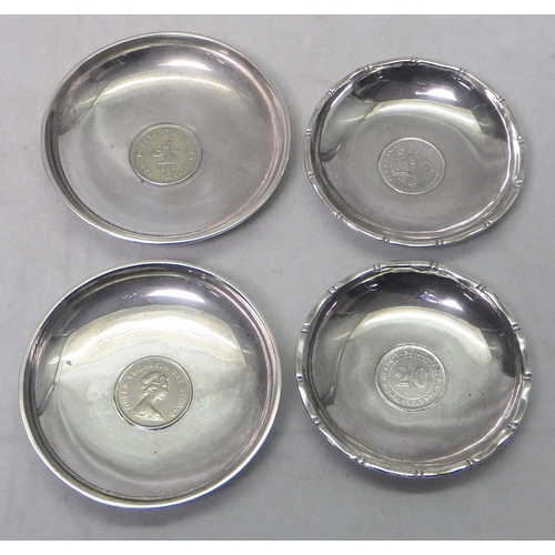 2 - Seven matching nut dishes each set with a central coin, white metal marked Sterling, 75mm diameter; ... 