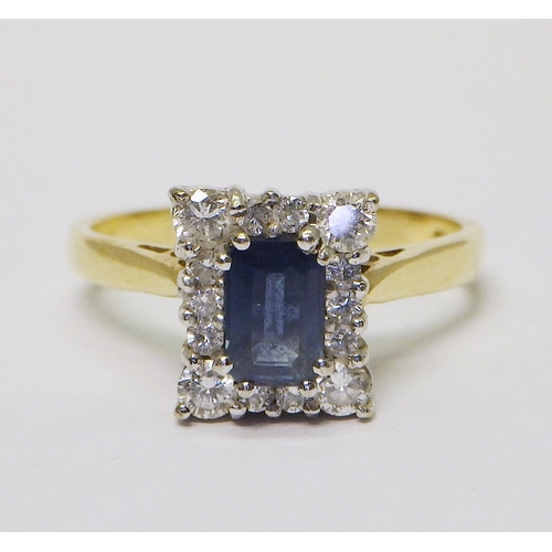 An 18ct gold diamond and sapphire cluster ring comprising 14 brilliant cut diamonds around an emerald cut sapphire.  Sapphire 5.5 x 3.5mm / 5g gross. Size O 1/2.