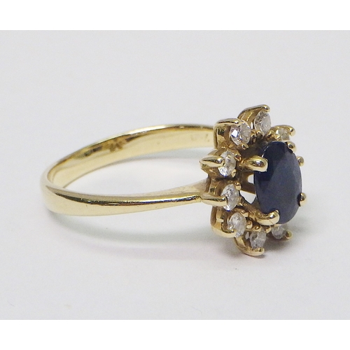 32 - A cluster ring comprising 10 brilliant cut diamonds around an oval cut sapphire, unmarked yellow met... 