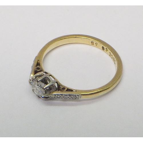 33 - A solitaire ring comprising a brilliant cut diamond within diamond set shoulders in a yellow metal s... 