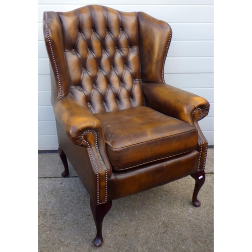 A brown buttoned leather wingback armchair