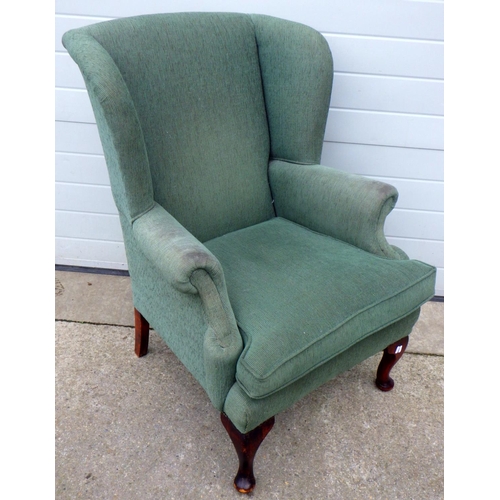 782 - A green upholstered wingback armchair, marks