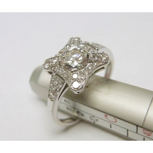An Art Deco influence cluster plaque ring comprising a central round cut diamond with a diamond surround and diamond set shoulders in an unmarked white metal setting and shank.  Central stone approximately 5.5mm diameter /plaque head approximately 14mm across diagonal / size M