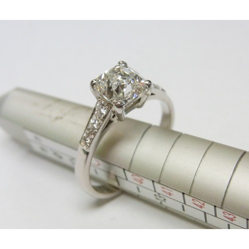32 - A solitaire ring comprising an old cushion cut diamond with diamond shoulders in a platinum claw set...