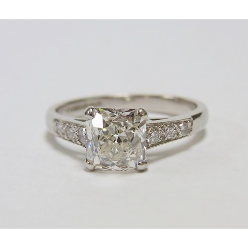 32 - A solitaire ring comprising an old cushion cut diamond with diamond shoulders in a platinum claw set... 