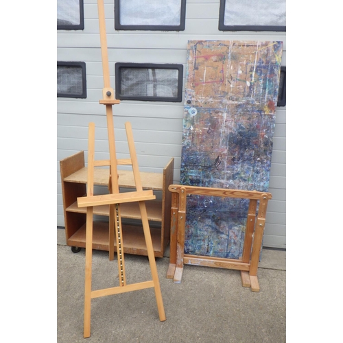 694 - An easel, pair of trestles and board and a wooden book trolley (5)