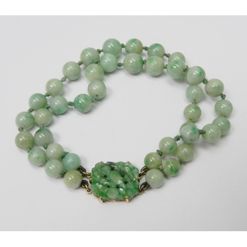 83 - A jade bracelet comprising two strands of graduated round beads with a carved plaque and yellow meta... 