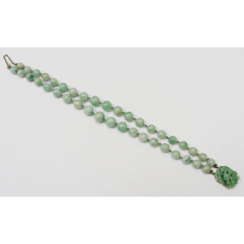 83 - A jade bracelet comprising two strands of graduated round beads with a carved plaque and yellow meta... 