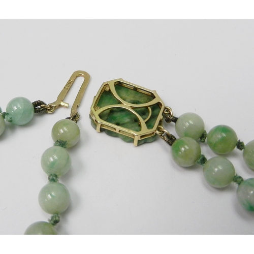 83 - A jade bracelet comprising two strands of graduated round beads with a carved plaque and yellow meta... 