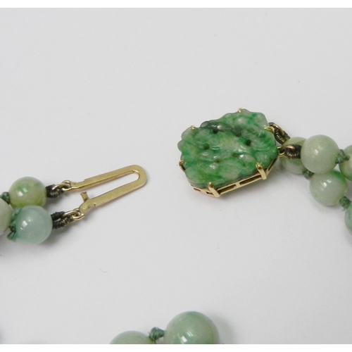 83 - A jade bracelet comprising two strands of graduated round beads with a carved plaque and yellow meta... 