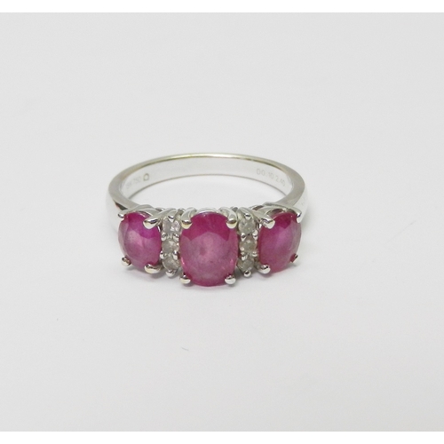 137 - A trilogy style ring comprising three graduated oval cut pink sapphires spaced with two pairs of rou... 