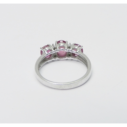 137 - A trilogy style ring comprising three graduated oval cut pink sapphires spaced with two pairs of rou... 