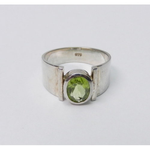 42 - A modernist art jewellery dress ring set with a single peridot  stone in a rub-over setting, white m... 