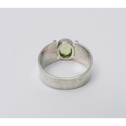 42 - A modernist art jewellery dress ring set with a single peridot  stone in a rub-over setting, white m... 