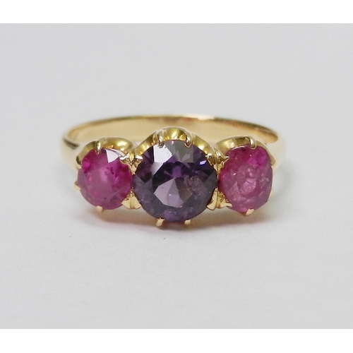 A trilogy ring, unmarked yellow metal set with a central amethyst flanked by two rubies.  Rubies a/f both chipped.  Central stone approx 5mm diameter.