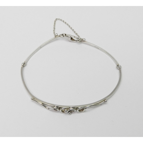 34 - A bangle of part articulated design having a central applied twist / loop motif, platinum bearing Sh... 