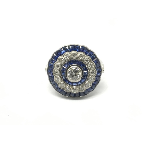 762 - A large platinum ring set with a central old cut diamond surrounded by calibre cut sapphires, a halo... 