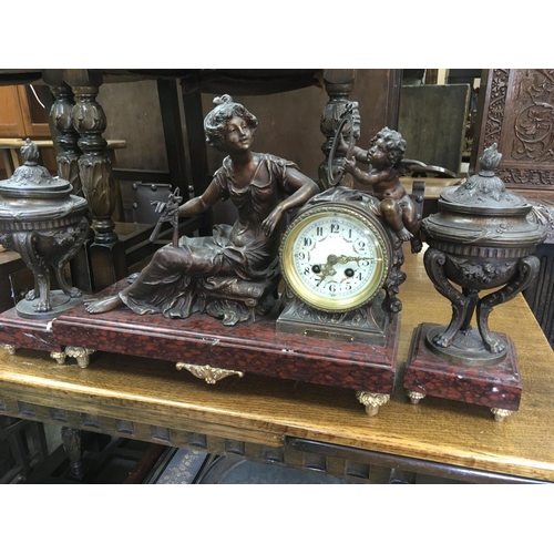 1317 - A spelter clock of classical form in the form of maiden and cherub with a matching pair of vases .