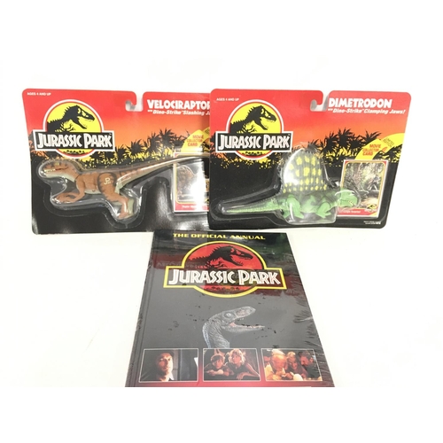 57 - 2 Carded Jurassic Park Figures and a sealed Annual. Including A Velociraptor and a Dimetrodon.