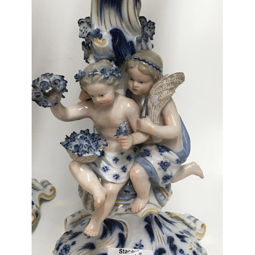 932 - A pair of Meissen candelabra with blue, white and gilt decoration o mounted with putti. 50cm. (Some ... 