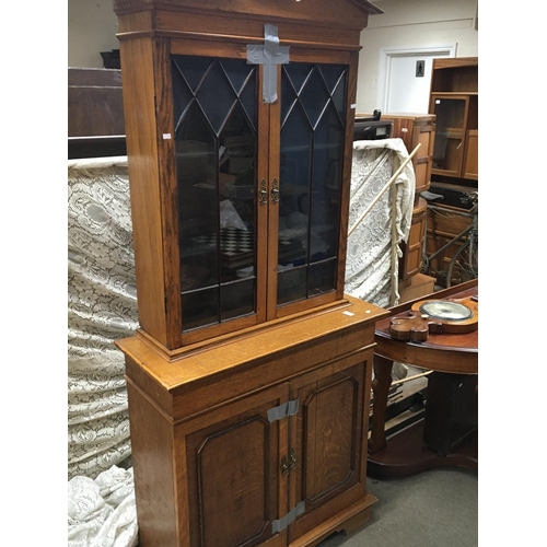 209 - A light oak bookcase with a shaped pediment above glazed doors and cupboards. NO RESERVE