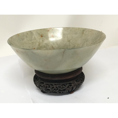 1041 - A 19th century Chinese green jade bowl with a carved hardwood stand. The bowl with stress cracks pos... 