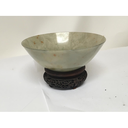 1041 - A 19th century Chinese green jade bowl with a carved hardwood stand. The bowl with stress cracks pos... 